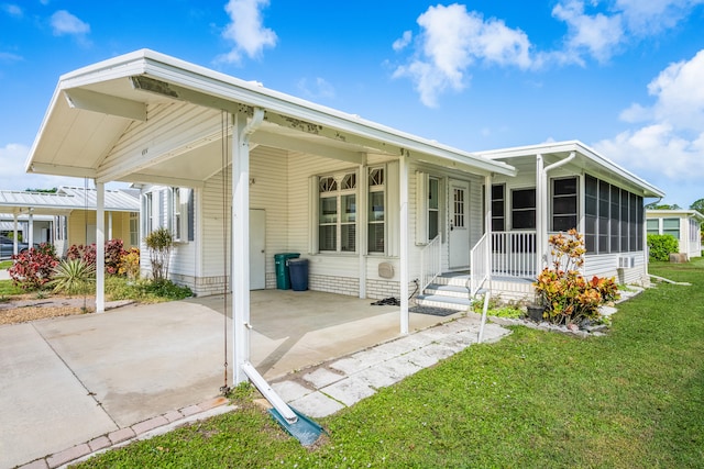 rear view of property featuring a sunroom, a lawn, and a carport