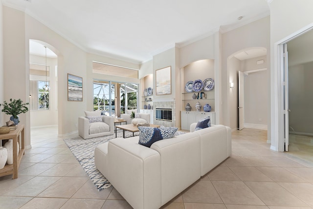 living area featuring light tile patterned floors, built in features, baseboards, a tiled fireplace, and ornamental molding