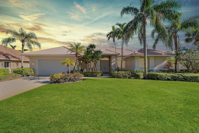 view of front of house featuring a garage, driveway, a lawn, a tiled roof, and stucco siding