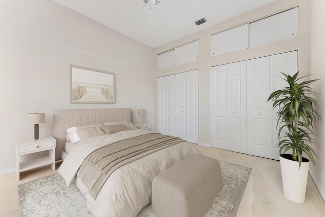 bedroom featuring multiple closets, light colored carpet, visible vents, and baseboards