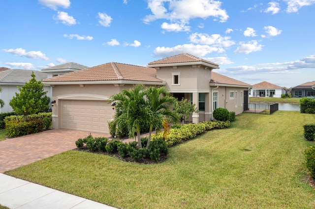 mediterranean / spanish-style house featuring a front lawn, a garage, a water view, decorative driveway, and stucco siding