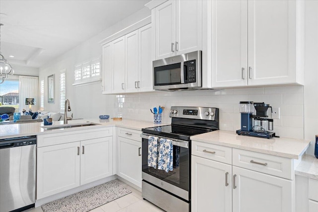 kitchen with a sink, stainless steel appliances, tasteful backsplash, light stone counters, and white cabinetry