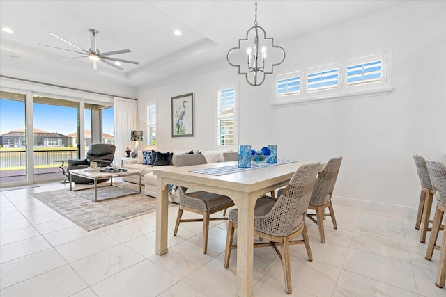 dining space with a wealth of natural light, ceiling fan with notable chandelier, and a raised ceiling