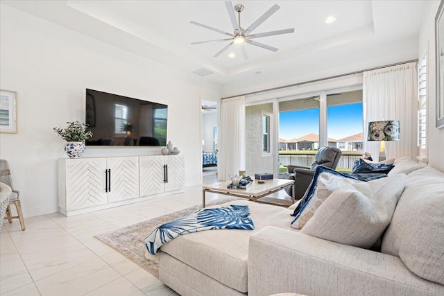 living room with a healthy amount of sunlight, a raised ceiling, a ceiling fan, and marble finish floor