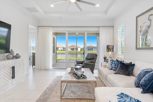 tiled living room with ceiling fan and a raised ceiling