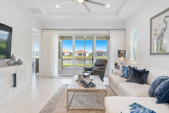 living area featuring a raised ceiling, ceiling fan, visible vents, and a water view