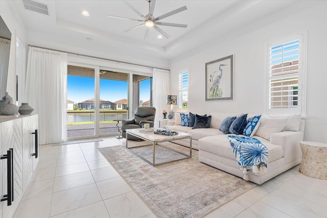 living area with plenty of natural light, a ceiling fan, visible vents, and a tray ceiling