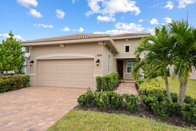 mediterranean / spanish-style house with a tiled roof, decorative driveway, a front yard, stucco siding, and a garage