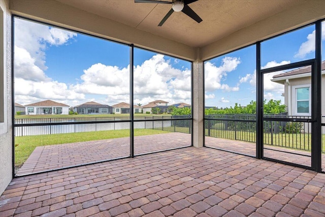 unfurnished sunroom featuring a residential view, ceiling fan, and a water view