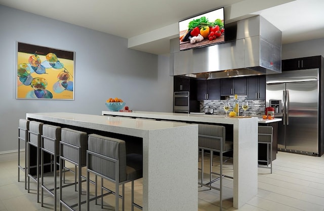 kitchen featuring tasteful backsplash, a breakfast bar, stainless steel appliances, a kitchen island, and wall chimney exhaust hood