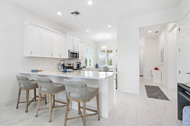 kitchen featuring kitchen peninsula, white cabinets, backsplash, appliances with stainless steel finishes, and a kitchen bar