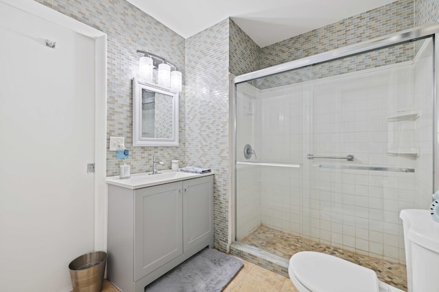 bathroom with tile patterned floors, vanity, tile walls, toilet, and a shower with shower door