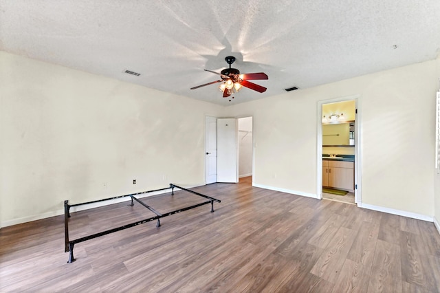 bedroom featuring a textured ceiling, ceiling fan, light hardwood / wood-style flooring, and ensuite bath