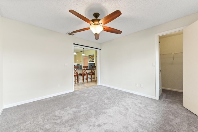 unfurnished bedroom with a walk in closet, a textured ceiling, ceiling fan, carpet floors, and a closet