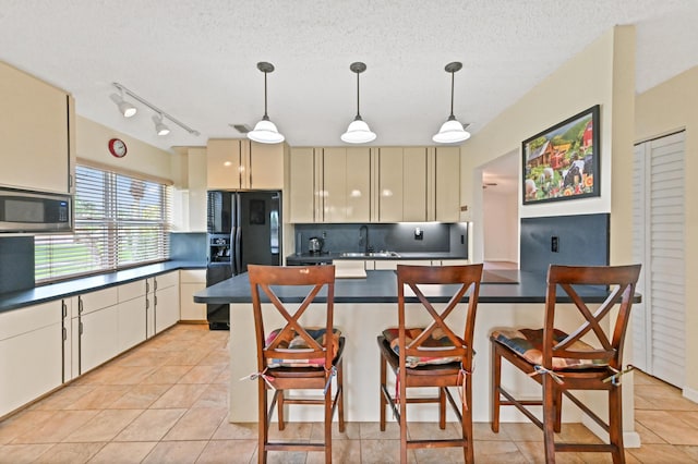 kitchen featuring pendant lighting, stainless steel microwave, cream cabinets, a kitchen breakfast bar, and black fridge with ice dispenser