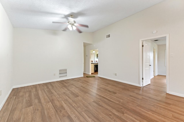 empty room featuring ceiling fan, a towering ceiling, a textured ceiling, and light hardwood / wood-style flooring