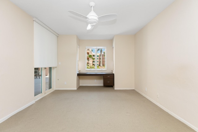 carpeted empty room featuring built in desk and ceiling fan