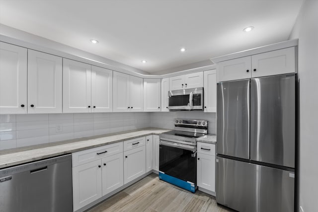 kitchen featuring decorative backsplash, white cabinets, light stone counters, light hardwood / wood-style floors, and stainless steel appliances