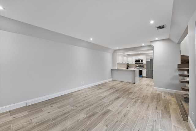 unfurnished living room featuring light hardwood / wood-style floors, sink, and vaulted ceiling