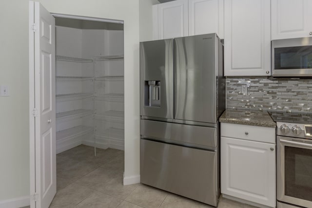 kitchen with light tile patterned floors, backsplash, white cabinetry, appliances with stainless steel finishes, and dark stone countertops