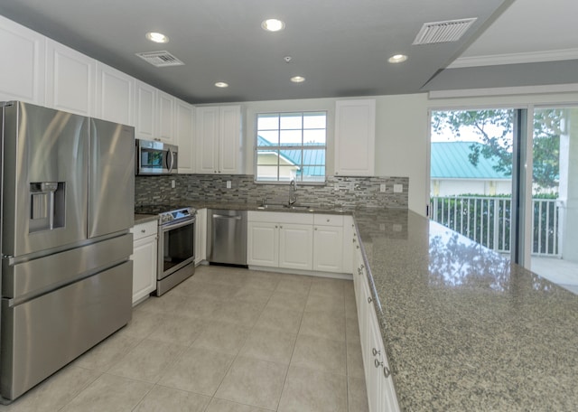 kitchen with stainless steel appliances, a healthy amount of sunlight, white cabinets, and tasteful backsplash