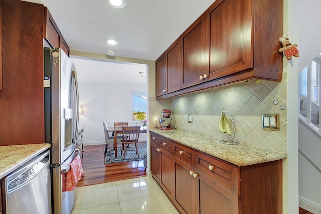 kitchen with a wealth of natural light, light stone countertops, appliances with stainless steel finishes, light hardwood / wood-style floors, and tasteful backsplash