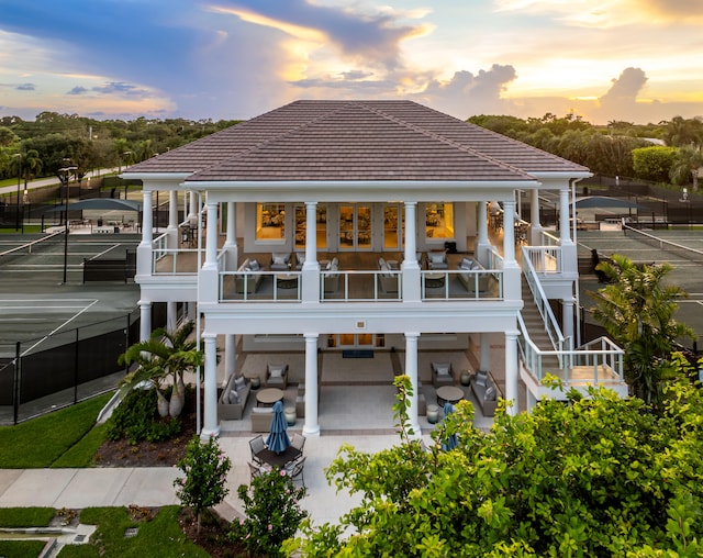 back house at dusk featuring a balcony and a patio area