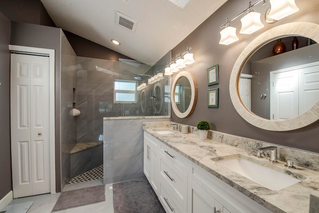 bathroom featuring a tile shower, a textured ceiling, vanity, and vaulted ceiling