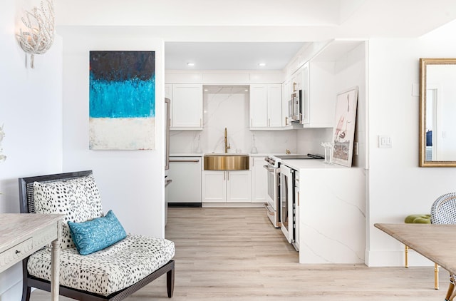 kitchen featuring backsplash, sink, appliances with stainless steel finishes, light hardwood / wood-style floors, and white cabinetry