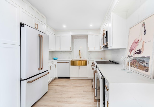 kitchen featuring appliances with stainless steel finishes, tasteful backsplash, sink, light hardwood / wood-style flooring, and white cabinets