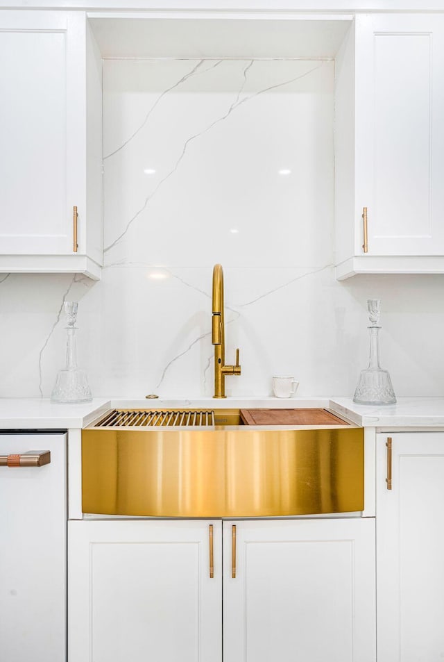 kitchen with white cabinetry, light stone counters, and sink