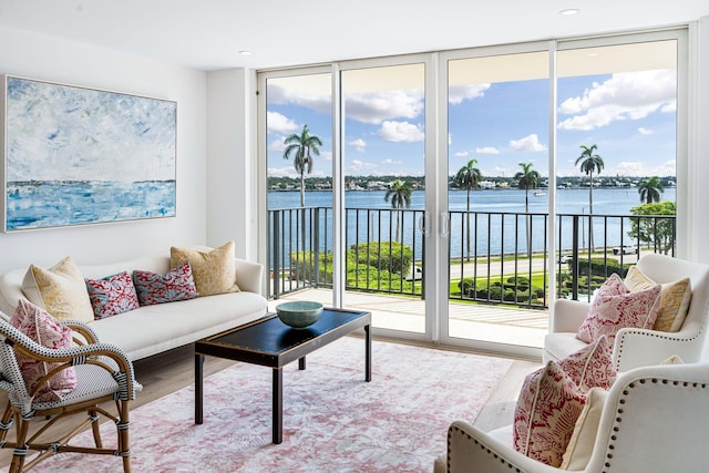 living room featuring a water view, light wood-type flooring, and a wall of windows