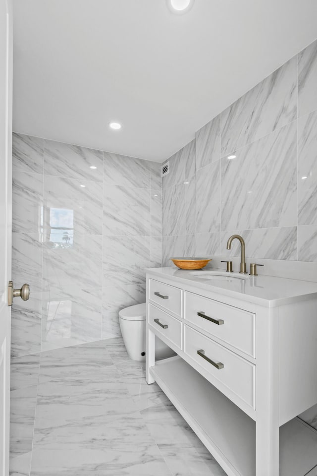 bathroom with vanity, toilet, and tile walls