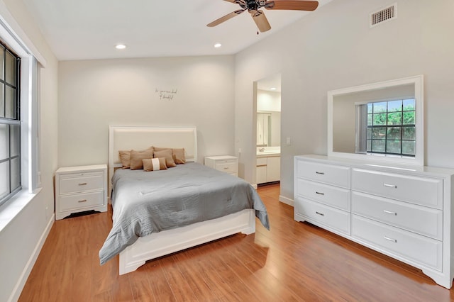 bedroom featuring light hardwood / wood-style floors, connected bathroom, vaulted ceiling, and ceiling fan