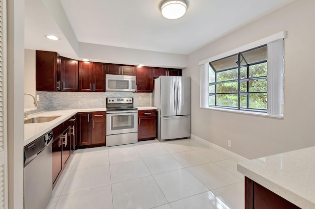 kitchen with tasteful backsplash, light stone countertops, appliances with stainless steel finishes, sink, and light tile patterned flooring