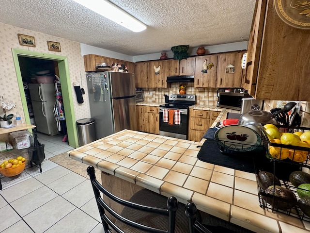 kitchen with tile countertops, a textured ceiling, stainless steel appliances, decorative backsplash, and light tile patterned floors