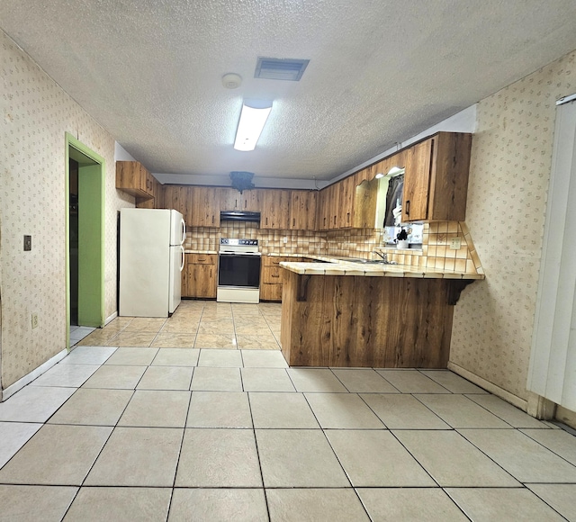 275 SE 16th Ave, Okeechobee, FL 34974 - kitchen with range with electric stovetop, freestanding refrigerator, a peninsula, wallpapered walls, and brown cabinetry