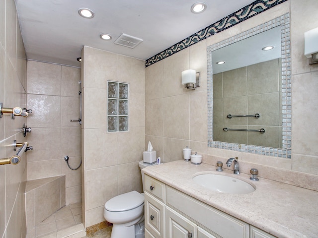 bathroom featuring vanity, tile patterned flooring, toilet, tile walls, and a tile shower