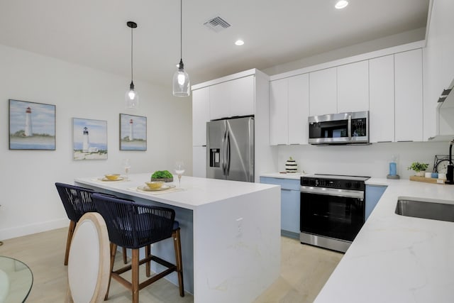 kitchen with white cabinets, hanging light fixtures, appliances with stainless steel finishes, light wood-type flooring, and a center island