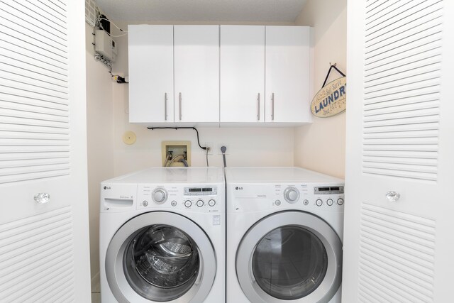 washroom featuring water heater, washer and clothes dryer, and cabinets