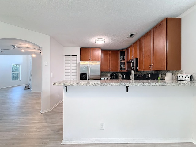 kitchen featuring kitchen peninsula, light wood-type flooring, appliances with stainless steel finishes, and tasteful backsplash