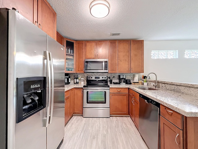 kitchen with sink, appliances with stainless steel finishes, tasteful backsplash, a textured ceiling, and light hardwood / wood-style flooring