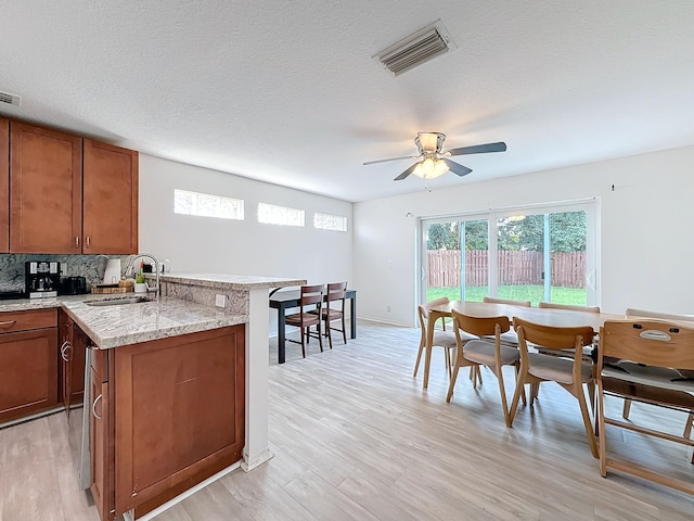 kitchen featuring a textured ceiling, decorative backsplash, sink, ceiling fan, and light hardwood / wood-style flooring