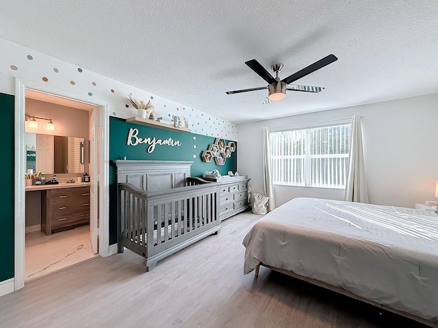 bedroom featuring light hardwood / wood-style floors, ceiling fan, connected bathroom, and a textured ceiling