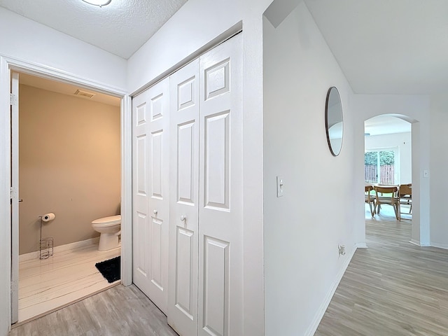 corridor with light hardwood / wood-style floors, a textured ceiling, and lofted ceiling