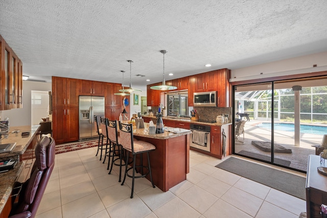 5609 SE Lamay Dr, Stuart, FL 34997 - kitchen featuring stainless steel appliances, a breakfast bar area, backsplash, light stone countertops, and decorative light fixtures