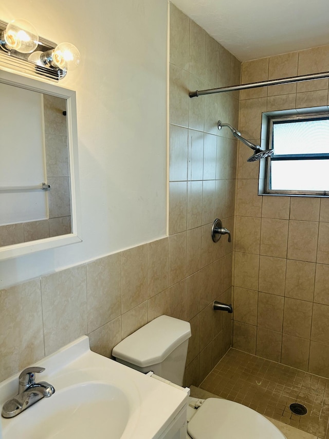 bathroom with tiled shower, wainscoting, toilet, vanity, and tile walls