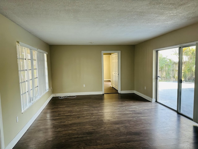 empty room with dark wood-type flooring, a textured ceiling, and baseboards