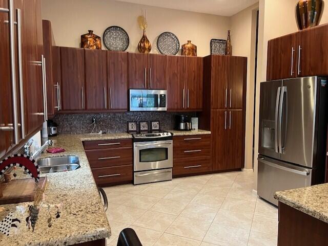 kitchen with sink, stainless steel appliances, light stone counters, backsplash, and light tile patterned floors