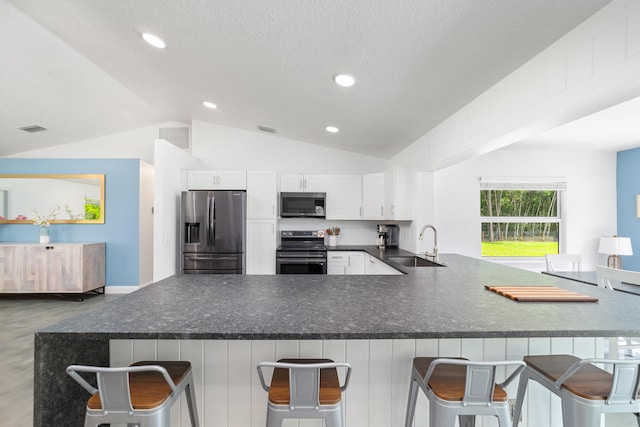 kitchen with lofted ceiling, a kitchen breakfast bar, kitchen peninsula, stainless steel appliances, and white cabinetry